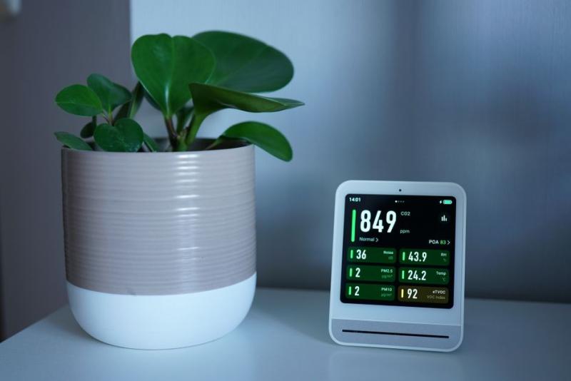 Pantalla de sensor de calidad del aire mostrando niveles de CO2 y PM2.5 junto a una planta